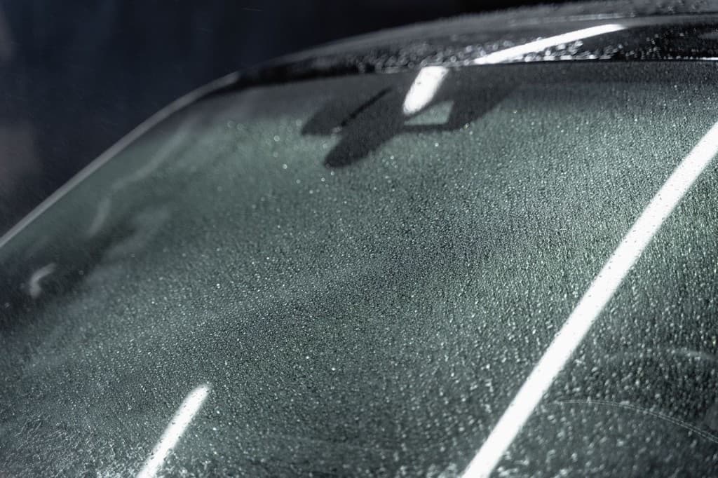 Close-up of a misted windshield showing the ADAS sensor and camera housing behind the glass