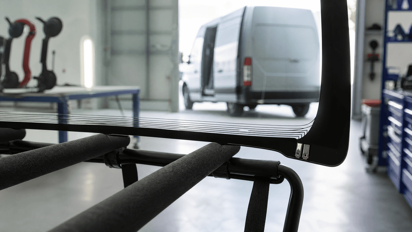 Lower edge of a new windscreen with a heated wiper park area and connector tabs on a rack in a UK glass workshop