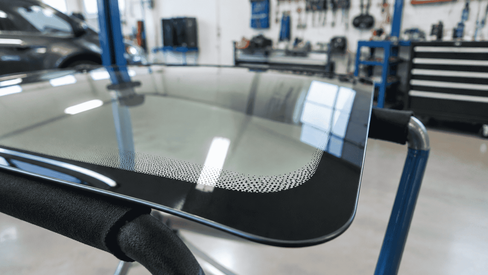 UK glass shop windscreen on a stand with soft workshop light, no readable markings visible